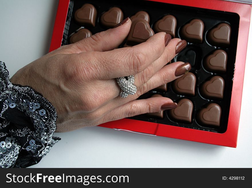 Female hand taking / holding a chocolate heart from a box. Female hand taking / holding a chocolate heart from a box