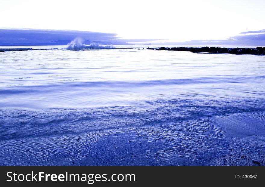 Early morning, blue tinted, image of a wave splashing up against the end of the tidal pool in St. James, Western Cape, South Africa. Early morning, blue tinted, image of a wave splashing up against the end of the tidal pool in St. James, Western Cape, South Africa.