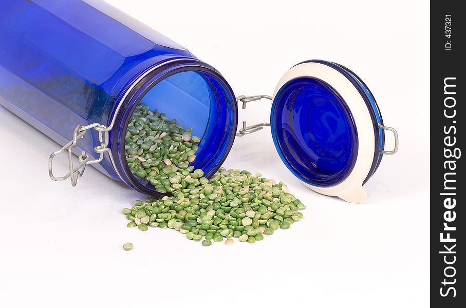 Dried split peas spilling out of a blue glass canister onto a white linen cloth. Dried split peas spilling out of a blue glass canister onto a white linen cloth