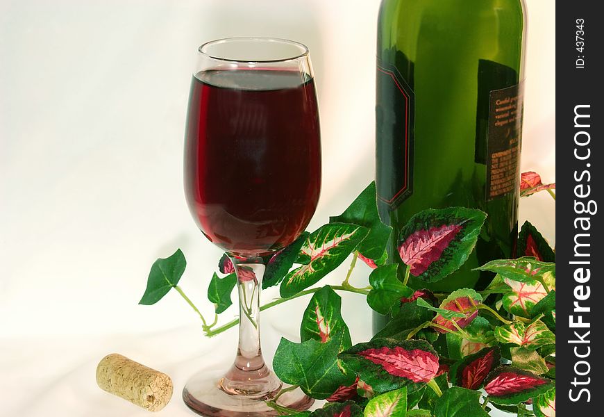 The last glass of delicious red wine next to an empty wine bottle, cork and colorful silk ivy against a white background. The last glass of delicious red wine next to an empty wine bottle, cork and colorful silk ivy against a white background.