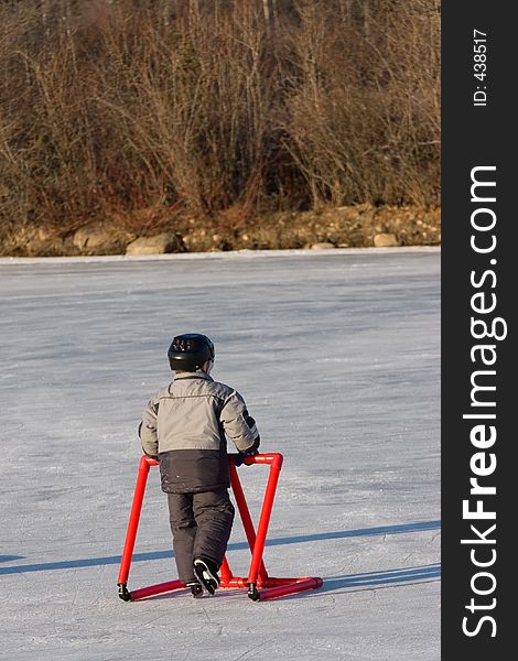 A young boy takes a leisurely skate while leaning on a learning tool for support. A young boy takes a leisurely skate while leaning on a learning tool for support.