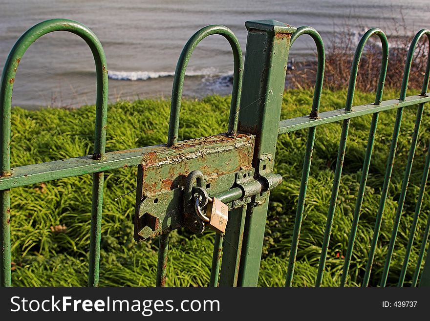 Padlock on green gate overlooking grass and sea. Padlock on green gate overlooking grass and sea.