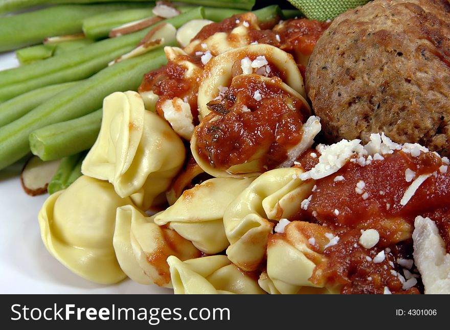 Tortellini and meatballs with sauce and green beans.