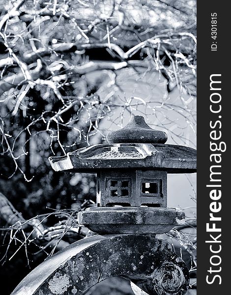 Cool toned black and white photo of a stone lantern in a Japanese garden.