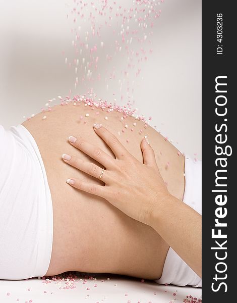 A pregnant woman's belly with pink anyseed falling on top of it.