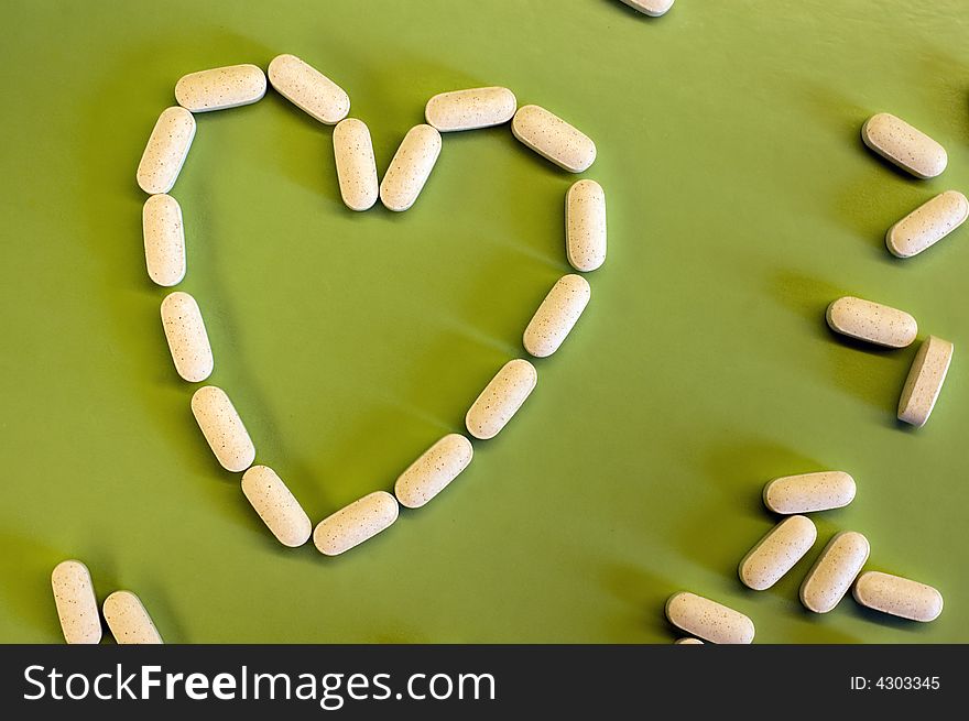 White pills on green background, heart shape