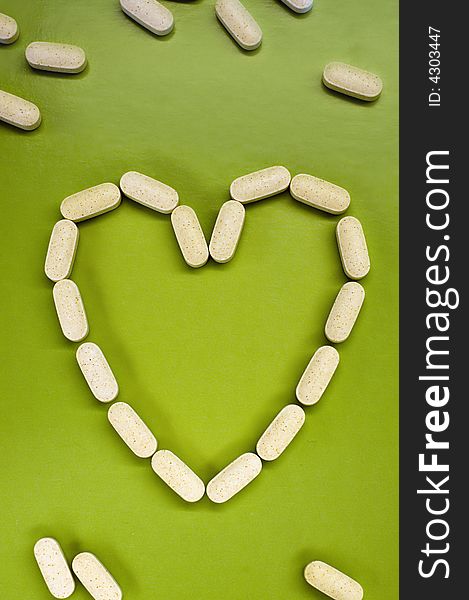 White pills on green background, heart shape