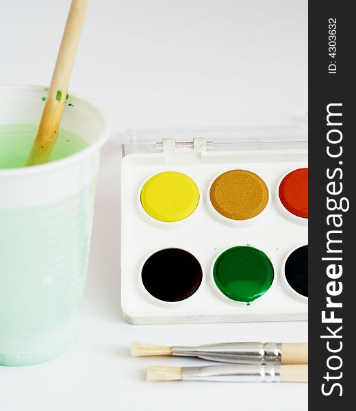 Water colors and brushes with water glass close-up studio shot on white background. Water colors and brushes with water glass close-up studio shot on white background