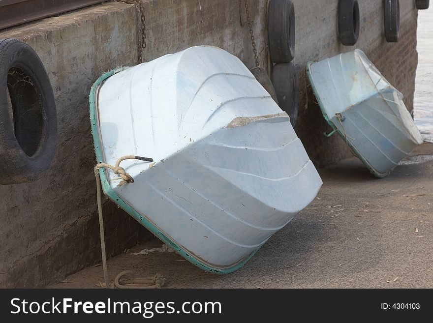 Small white and Jade Fishingboats with rope  in a row against sement wall with tyres and chains. Small white and Jade Fishingboats with rope  in a row against sement wall with tyres and chains