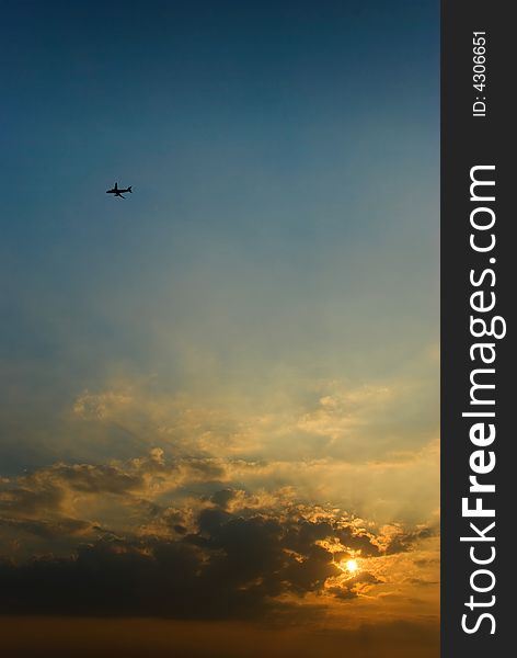 An aeroplane silhouetted in the sky as the sun rises over the horizon, partly obscured by low altitude clouds. An aeroplane silhouetted in the sky as the sun rises over the horizon, partly obscured by low altitude clouds