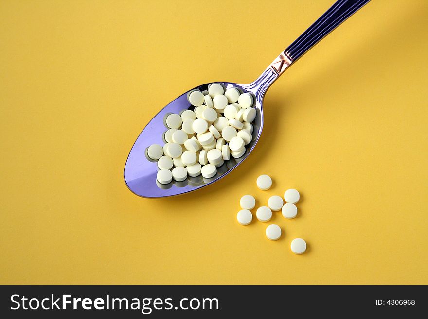 Spoon full of yellow pills isolated on yellow background. Spoon full of yellow pills isolated on yellow background.