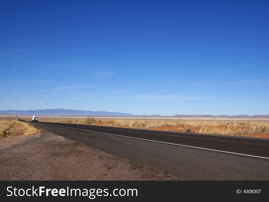 Lone truck travels Central New Mexico USA road with wide open spaces around and mountains in the far distance. Lone truck travels Central New Mexico USA road with wide open spaces around and mountains in the far distance.