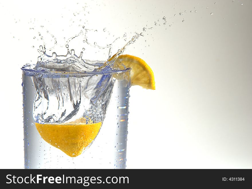 A lemon half splashing into a glass of water. A lemon half splashing into a glass of water.