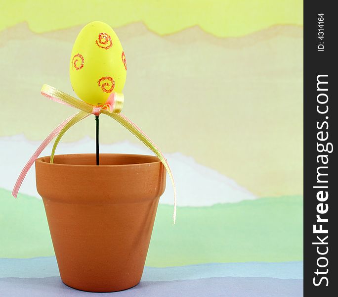 Yellow decorated Easter egg in a terracotta flowerpot on a pastel colored background. Yellow decorated Easter egg in a terracotta flowerpot on a pastel colored background.