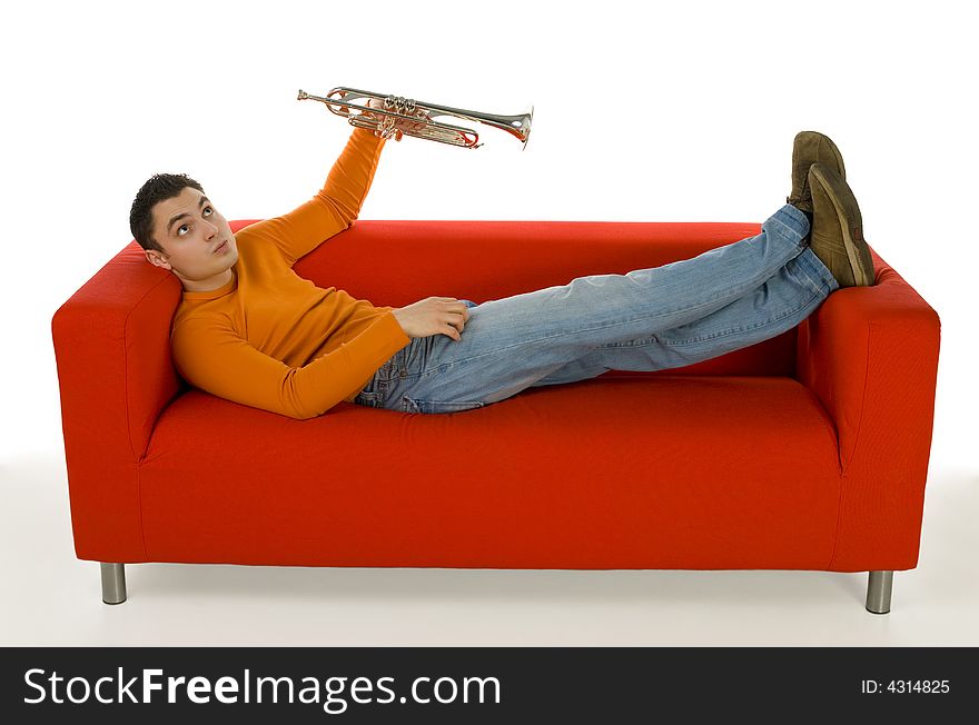 Thoughtful trumpeter lying on red couch and holding trumpet in hand. He's looking at something up. White background.