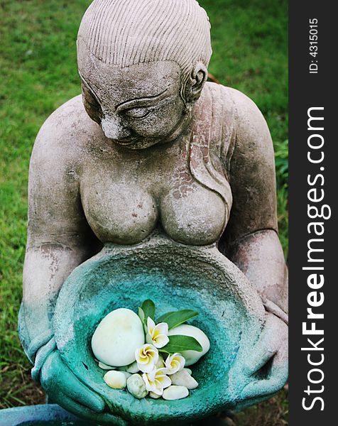 Asian statue holding a bowl of fragapani flowers - focus on the face.