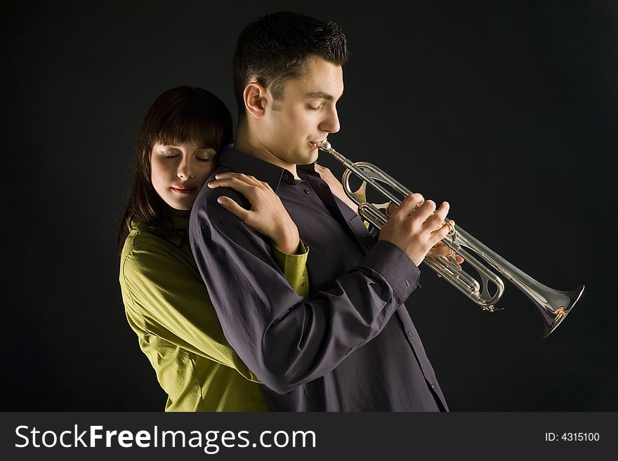 The woman huging the trumpet man. She standing behind the man. Side view. The woman huging the trumpet man. She standing behind the man. Side view.