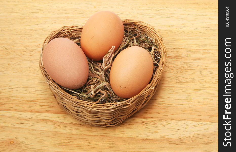 Three eggs in a wicker  basket on a wooden surface. Three eggs in a wicker  basket on a wooden surface
