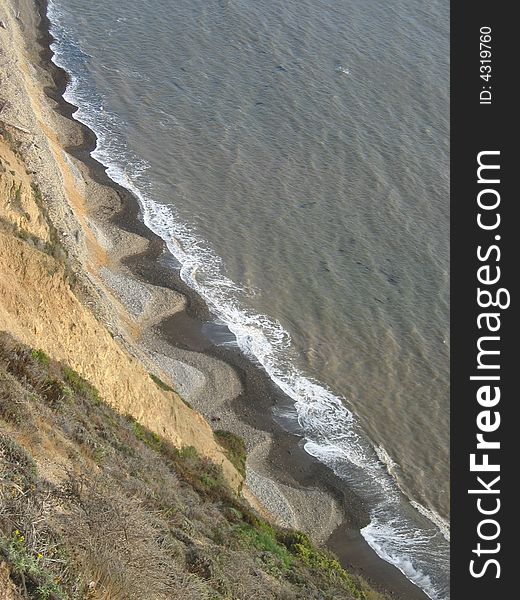 Waves washing ashore at the base of a cliff leaving an's' shaped line of wet sand on the beach. Waves washing ashore at the base of a cliff leaving an's' shaped line of wet sand on the beach