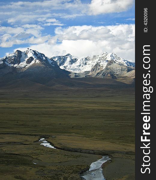 Vertical format shot with a meandering stream on a plain leading to a group of snow-capped mountain peaks. Vertical format shot with a meandering stream on a plain leading to a group of snow-capped mountain peaks