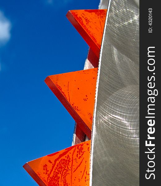 Abstract shot of orange and brushed aluminum set against a bright blue sky. Vertical format