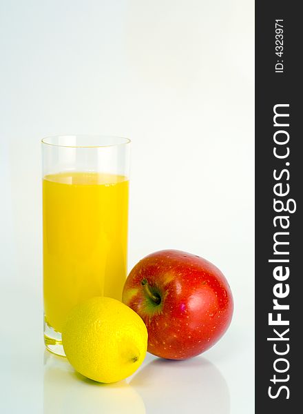 Big transparent glass of orange juice, yellow lemon, red apple on white background. Big transparent glass of orange juice, yellow lemon, red apple on white background