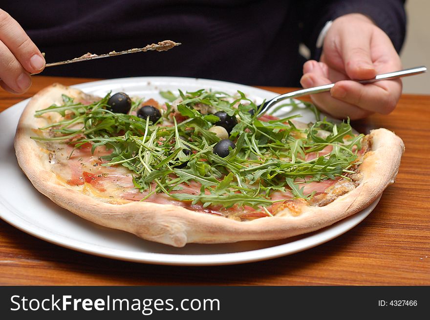 Vegetable pizza with ruccola and olives, mans hands holding  knife and fork, detail. Vegetable pizza with ruccola and olives, mans hands holding  knife and fork, detail.