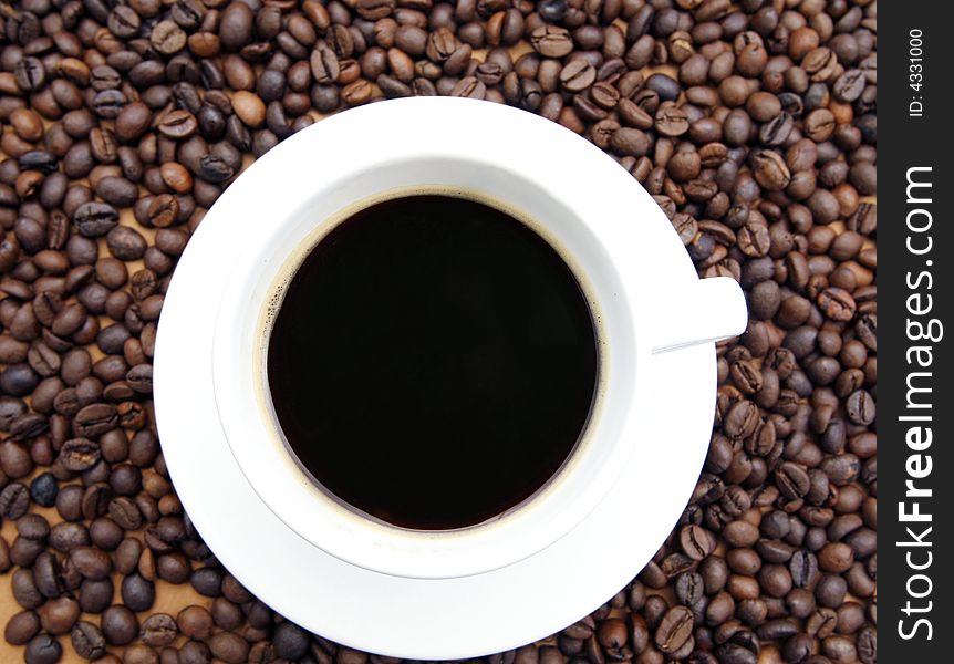 White coffee cup with black coffee and coffee beans on brown background