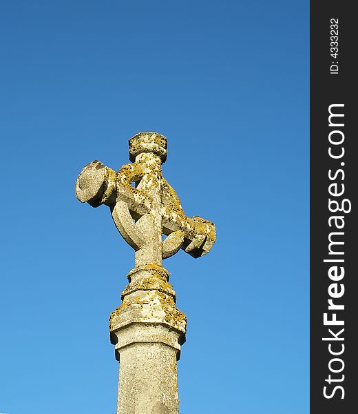 Lichen covered celtic cross set against blue sky
