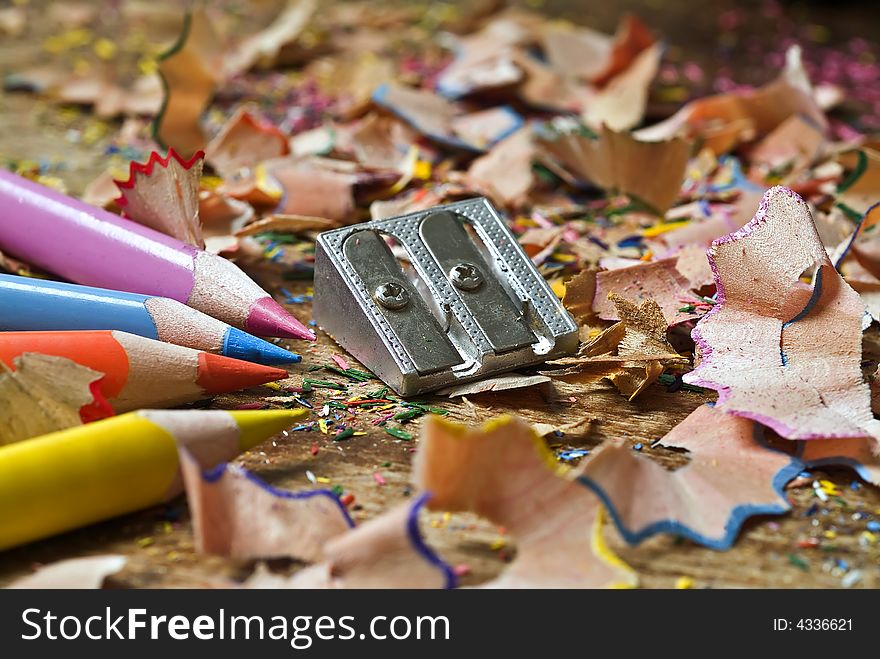 Colored pencils sharpener and shavings on wooden surface