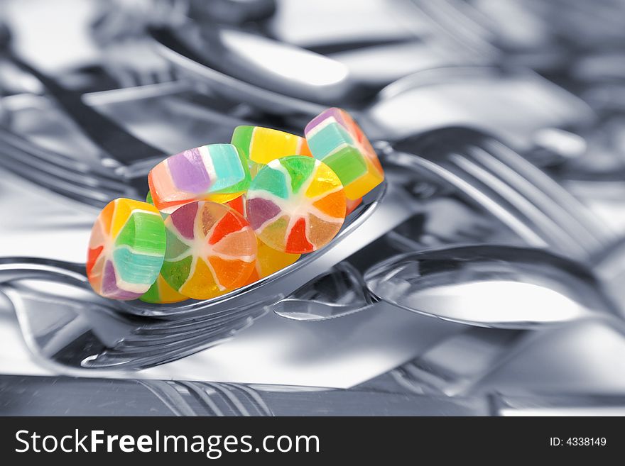 Colorful candy wheels sit on a spoon in a sea of utensils.  Silverware is black and white and candies are selectively colored. Colorful candy wheels sit on a spoon in a sea of utensils.  Silverware is black and white and candies are selectively colored.