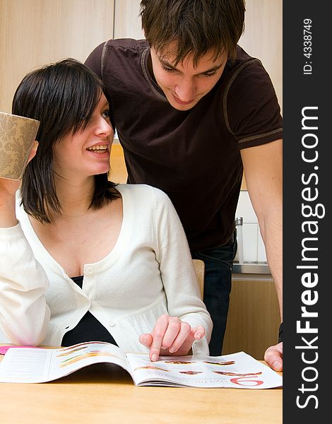 Young happy couple reading magazine in the kitchen. Young happy couple reading magazine in the kitchen