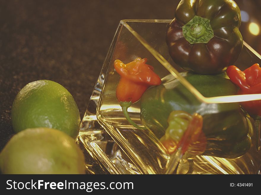 Vegatables and fruit, lemons, peppadews and greenpeppers in a squire shine through glass flower pot on black marble surface to front. Vegatables and fruit, lemons, peppadews and greenpeppers in a squire shine through glass flower pot on black marble surface to front