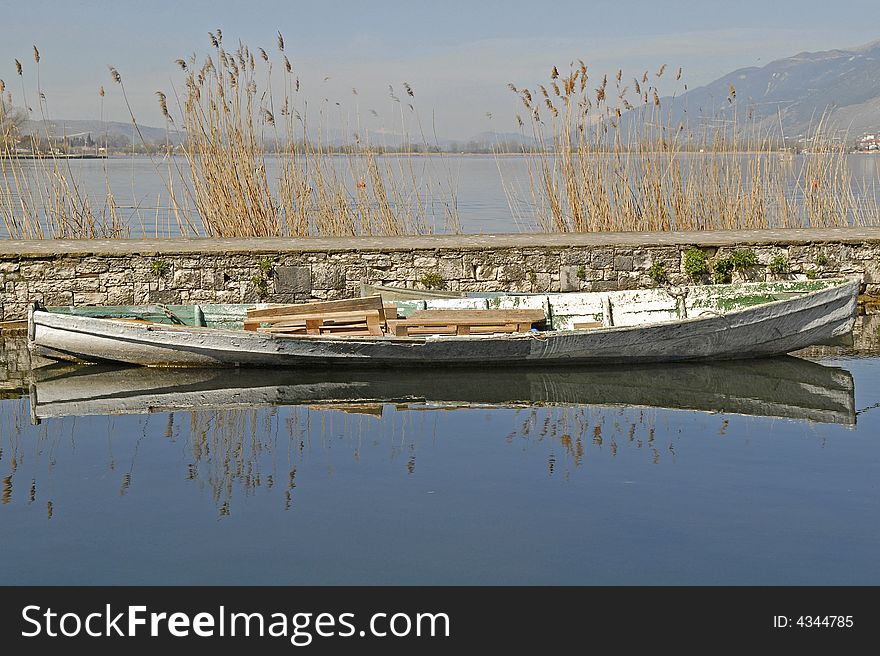 An old boat and its reflection on the water. grass, lake and the sky as background. An old boat and its reflection on the water. grass, lake and the sky as background