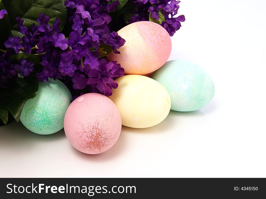 Colorful pastel Easter eggs next to purple spring silk flowers on white background. Colorful pastel Easter eggs next to purple spring silk flowers on white background