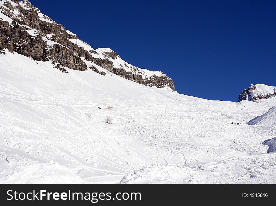 A picture of a snowy mountain side covered in ski tracks with a small group of skiers and a deep blue sky. A picture of a snowy mountain side covered in ski tracks with a small group of skiers and a deep blue sky