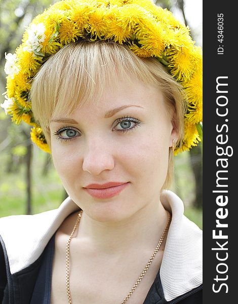 The young girl with a wreath from dandelions on a head