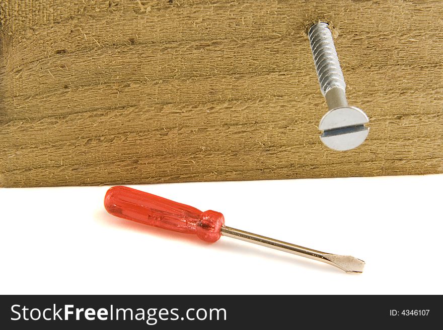A very small screwdriver lying on a white surface next to a large screw, screwed into a vertical piece of wood