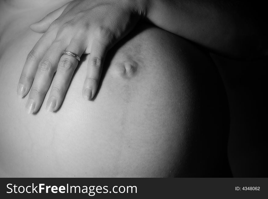 A pregnant woman wearing a wedding band places her hand over her belly. A pregnant woman wearing a wedding band places her hand over her belly.