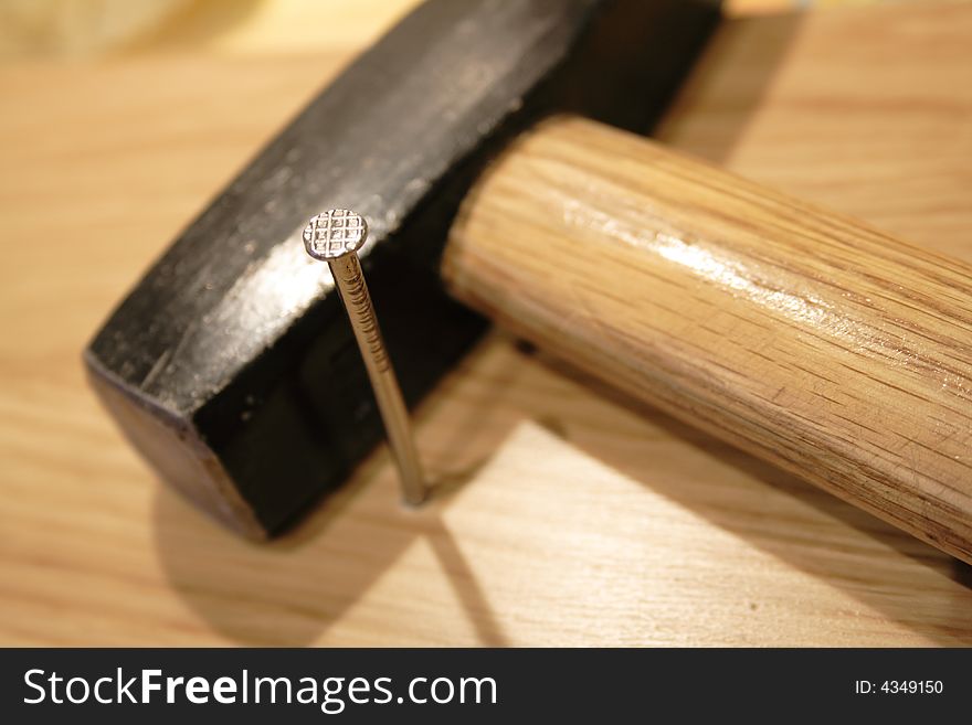 Driven-in nail and hammer on wooden background