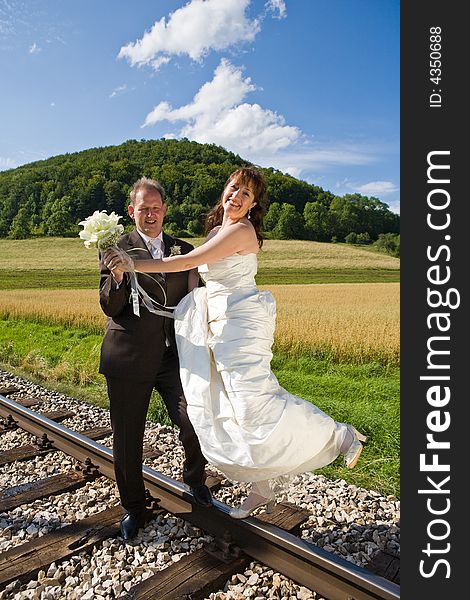 Bridal couple on rails, being in the nature. Great azure sky. Great summer! She balances on one foot on the rail.
