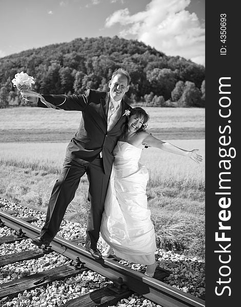 Bridal couple on rails, being in the nature. Great azure sky. Great summer! He balances with one foot on the rail. Black-white, monochrome. Bridal couple on rails, being in the nature. Great azure sky. Great summer! He balances with one foot on the rail. Black-white, monochrome.