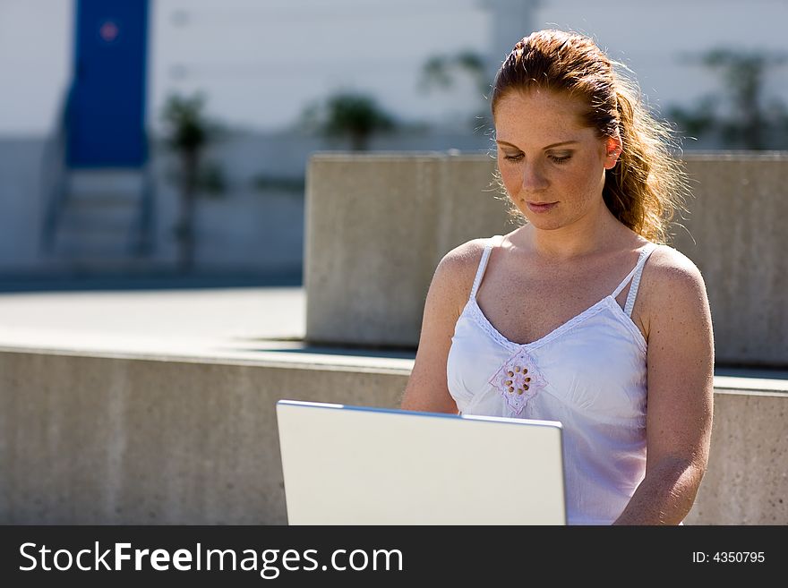 Woman (a scholar?) sitting alone on a stair, typing on the silver laptop. It's lightish and summery. Woman (a scholar?) sitting alone on a stair, typing on the silver laptop. It's lightish and summery.