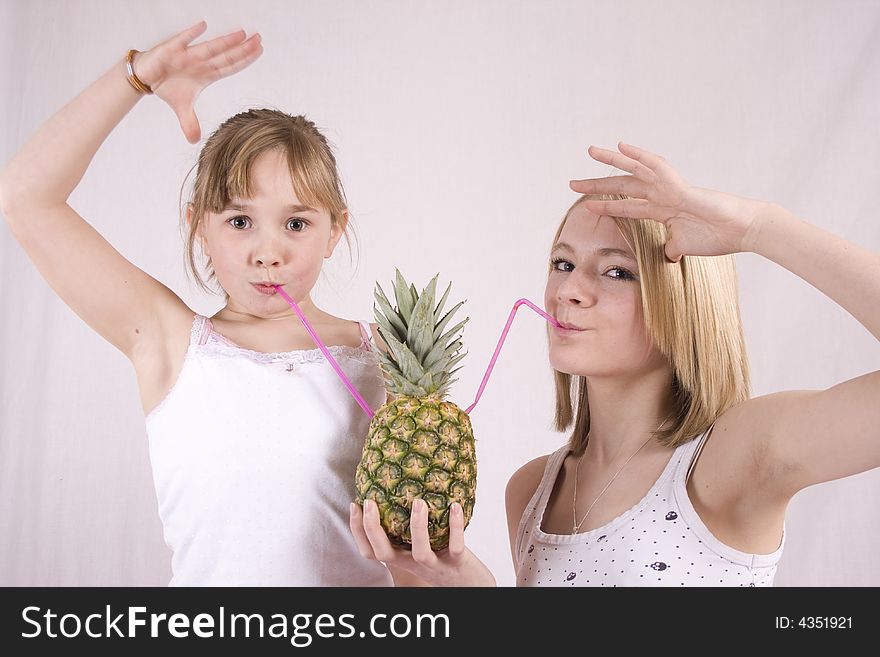 Two young girls with hands in the air   drinking from a pineapple. Two young girls with hands in the air   drinking from a pineapple