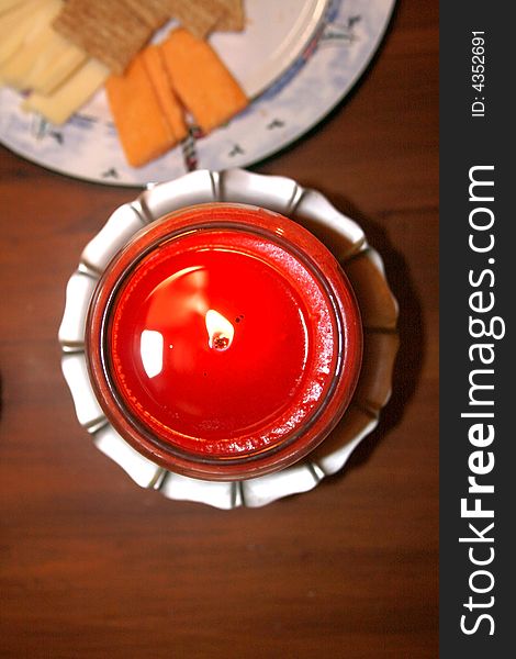 A plate of cheese and crackers waits next to a warm red candle. A plate of cheese and crackers waits next to a warm red candle.