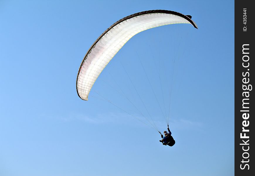 A paraglider is flying in the blue sky with his white paraglide. A paraglider is flying in the blue sky with his white paraglide