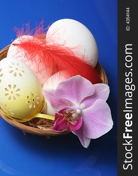 Easter eggs in basket with orchid on blue background.