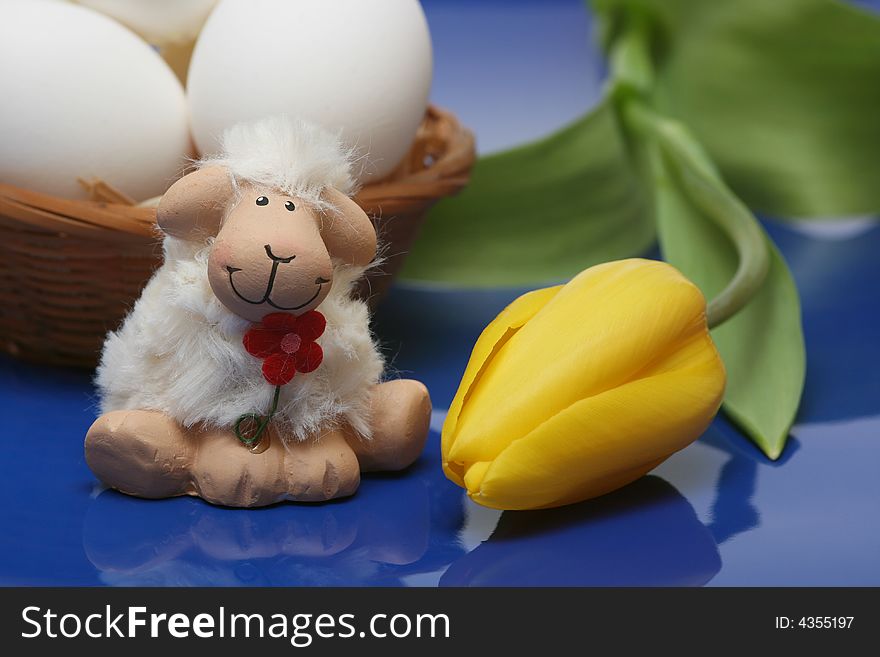 Easter motive.Easter lamb with yellow tulip,white eggs on blue background.