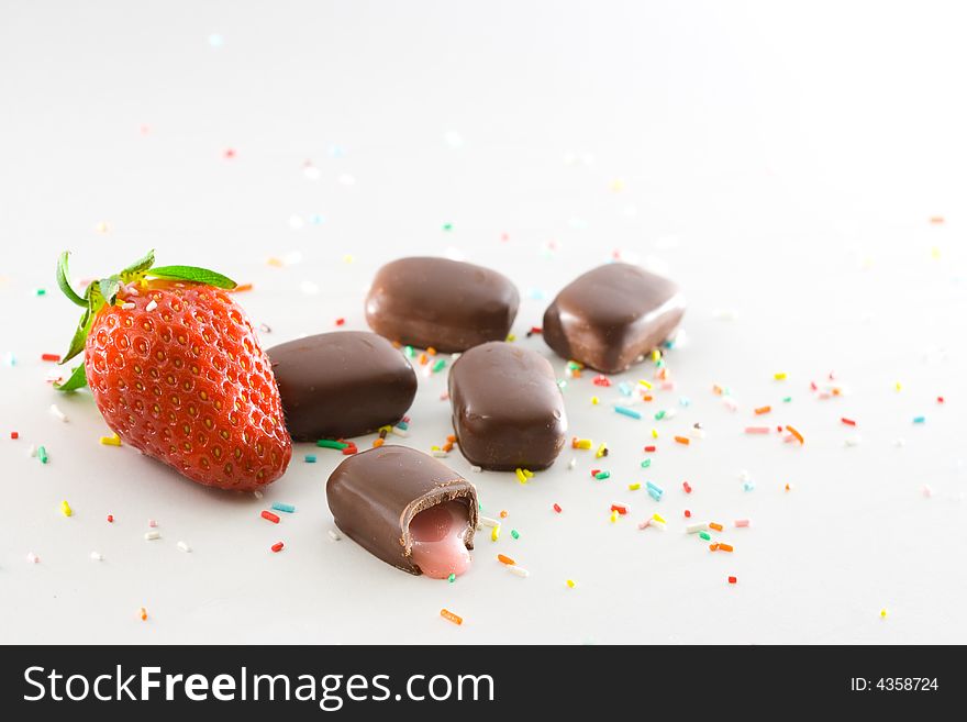 Strawberries, cream filled chocolates and colored candy confetti on white background. Strawberries, cream filled chocolates and colored candy confetti on white background.