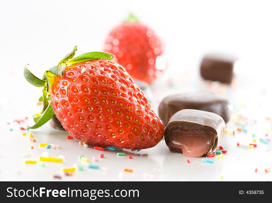 Strawberries, cream filled chocolates and colored candy confetti closeup on white background. Strawberries, cream filled chocolates and colored candy confetti closeup on white background.